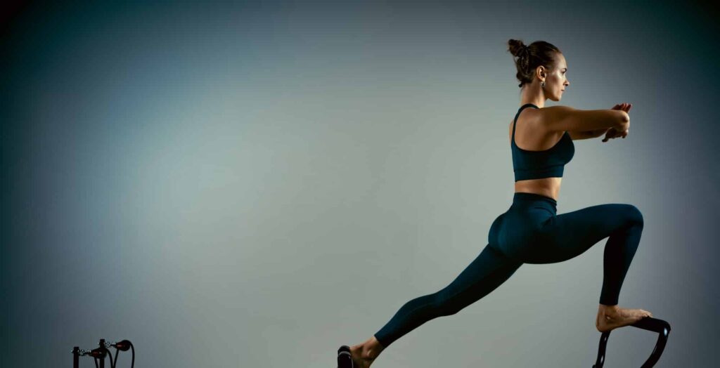 Young girl doing pilates exercises with a reformer bed. Beautiful slim fitness trainer on a reformer